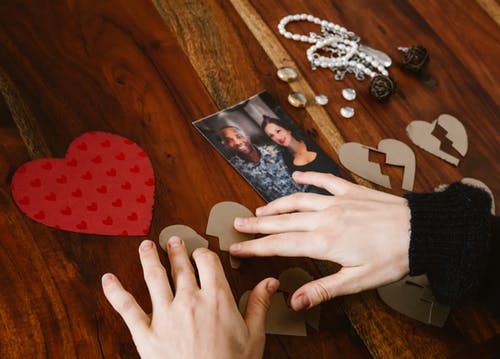 Twee kinderhanden die gebroken hartjes naast een foto van een man en een vrouw leggen