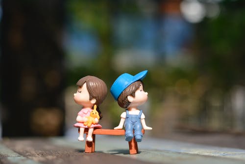 Twee kleine poppetjes op een bankje, een meisje en een jongetje die van elkaar wegkijken