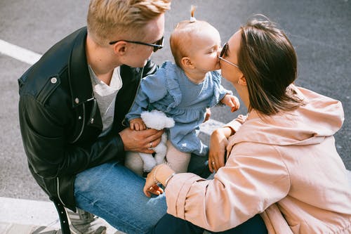 Baby bij vader op schoot krijgt kus van moeder