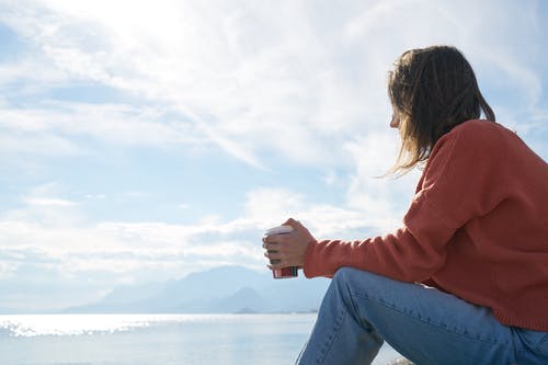 Een persoon die uitkijkt over het water met een beker koffie in de hand