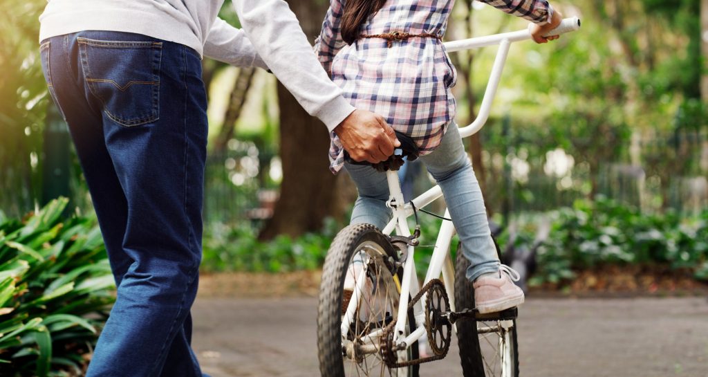 Een vader helpt zijn dochter om te leren fietsen