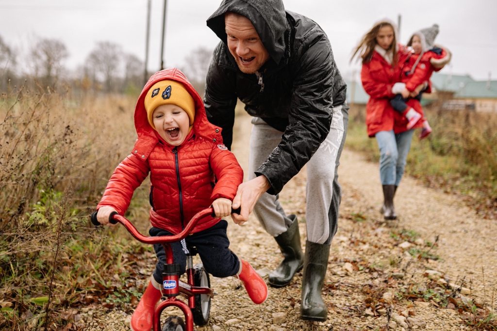 Gezin wandelt buiten in de regen en leert jongste kind fietsen